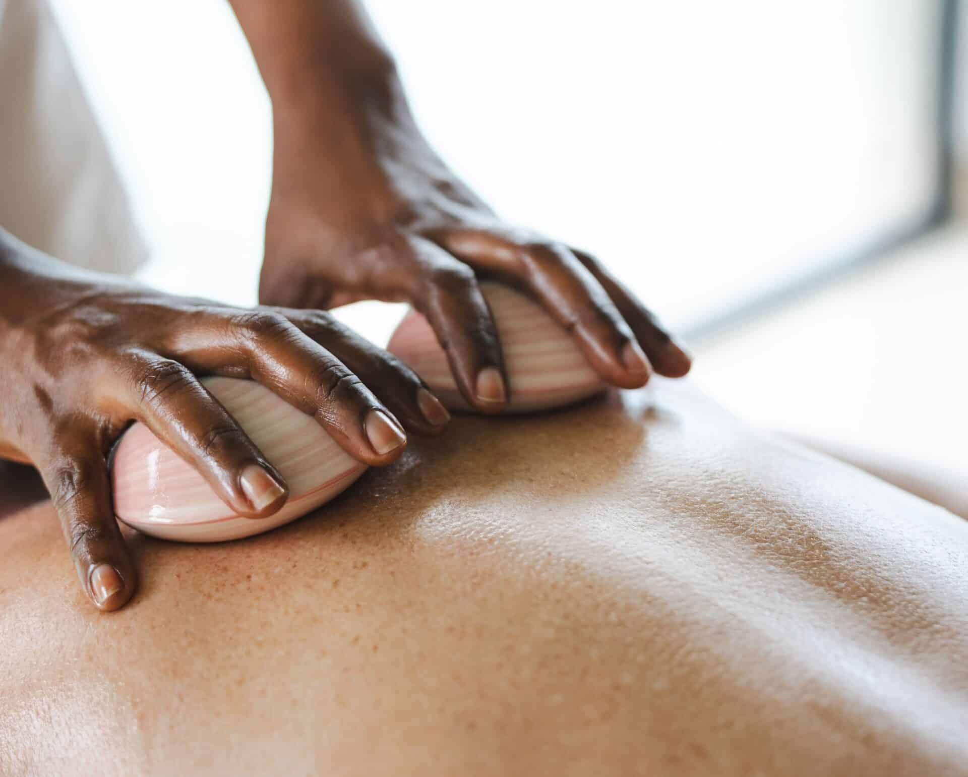 Close-up of a person receiving a back massage at Oil Nut Bay spa, with large seashells held in the therapist’s hands. The focus is on the therapist’s hands and shells gliding across the client’s back.