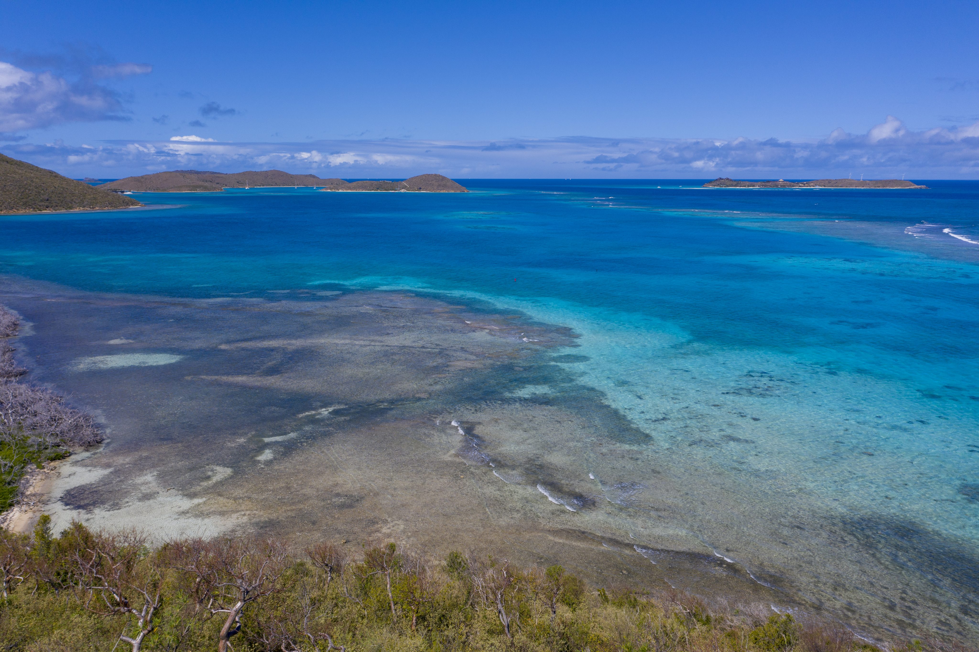 A tranquil seascape showcasing clear turquoise waters gently lapping against a sandy beach in the foreground, with lush green islands and rocky outcrops dotting the background under a bright blue sky, creating an idyllic setting for your dream estate.