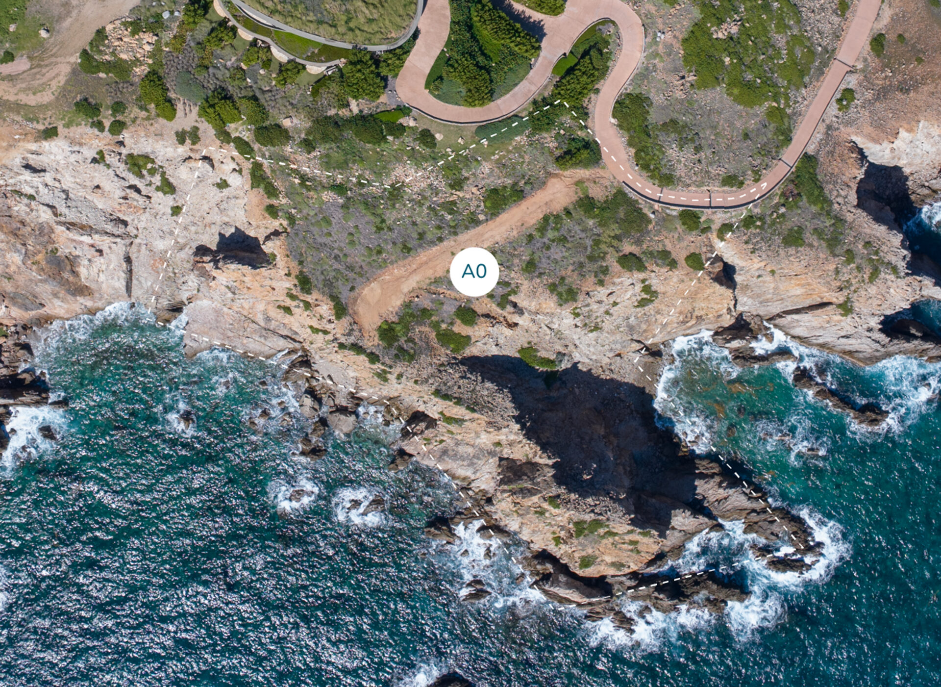 Aerial view of a rocky coastal area along the Atlantic Ridge, with waves crashing against the shore. A winding path runs through green vegetation atop the cliffs. A circular marker labeled "Homesite A0" is positioned in the middle. The ocean water is deep blue with white foam at the edges.