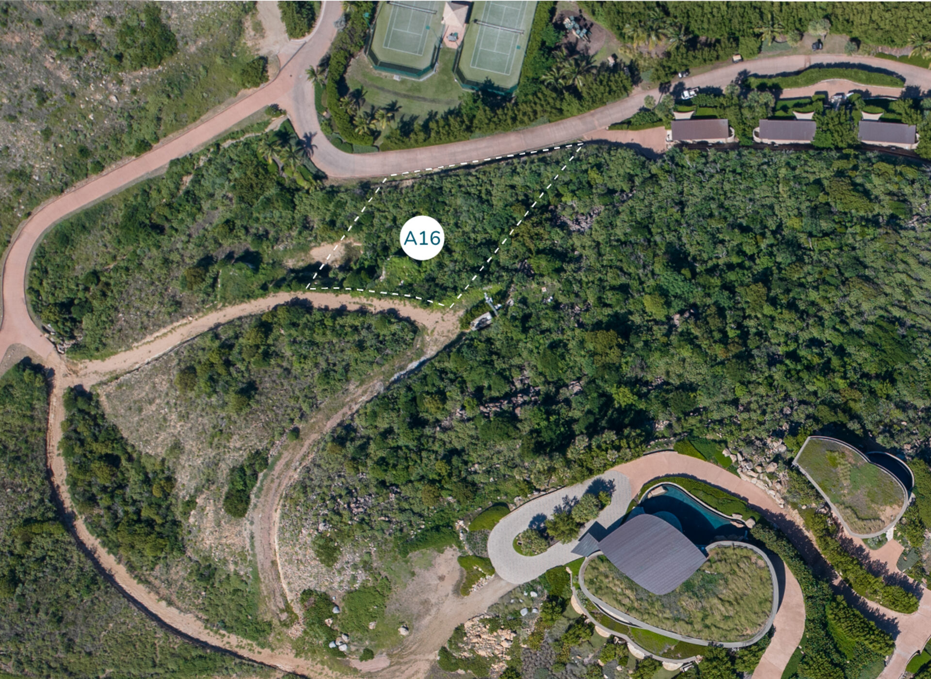 Aerial view of Homesite A16 at Atlantic Ridge, surrounded by dense foliage. Curved pathways and roads encircle the plot, with neighboring houses and tennis courts nearby.