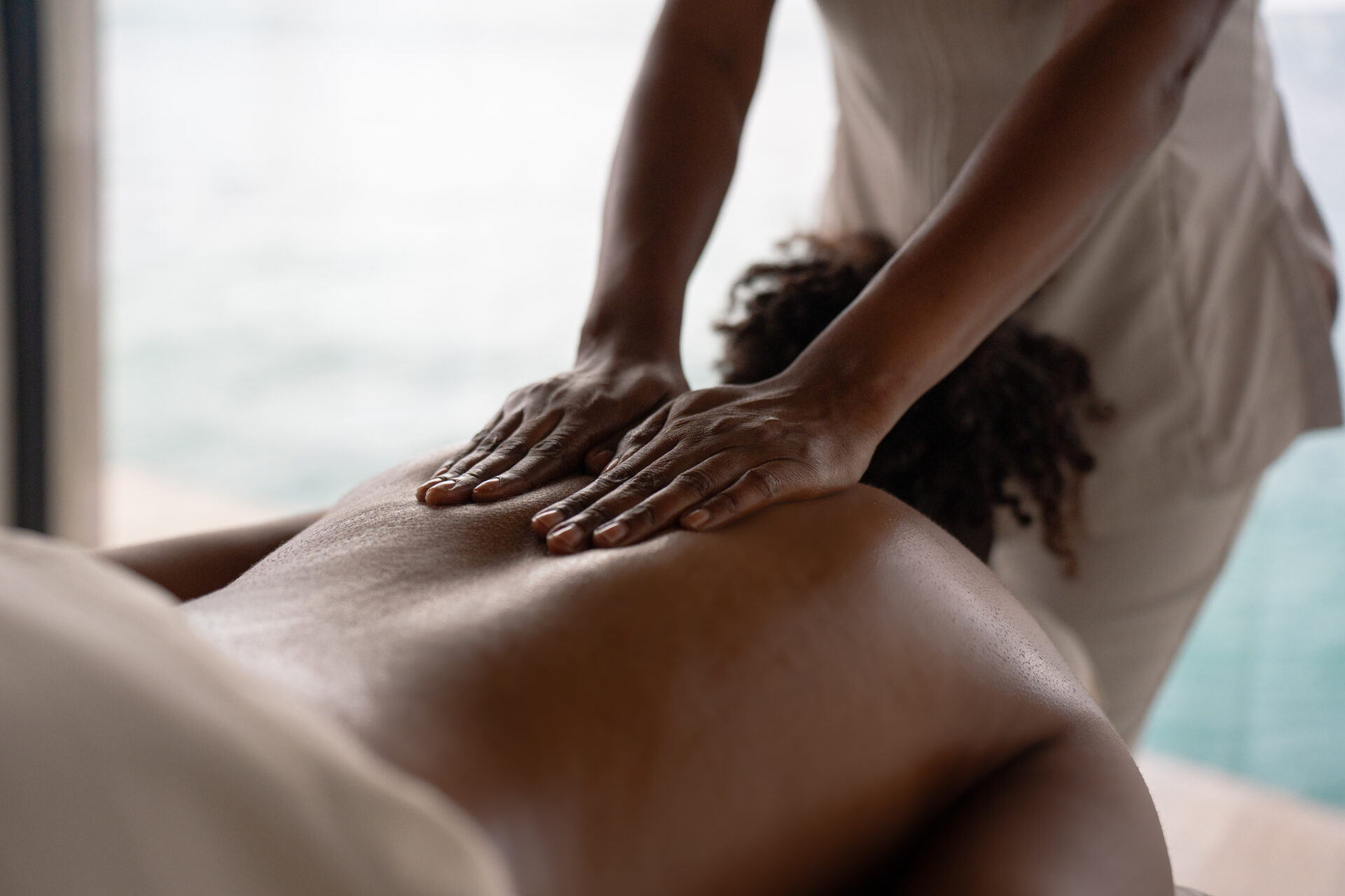 A person receives a relaxing back massage from a massage therapist at the Oil Nut Bay spa, who is pressing their hands gently on the client’s bare back in a serene, softly lit setting.