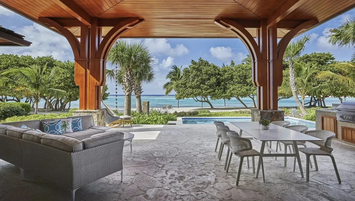 An expansive wooden-beamed pavilion houses a contemporary outdoor living and dining area. Stone flooring leads to a private pool and a "secluded" white-sand beach, where palm trees sway against the backdrop of the "vivid" Caribbean Sea.