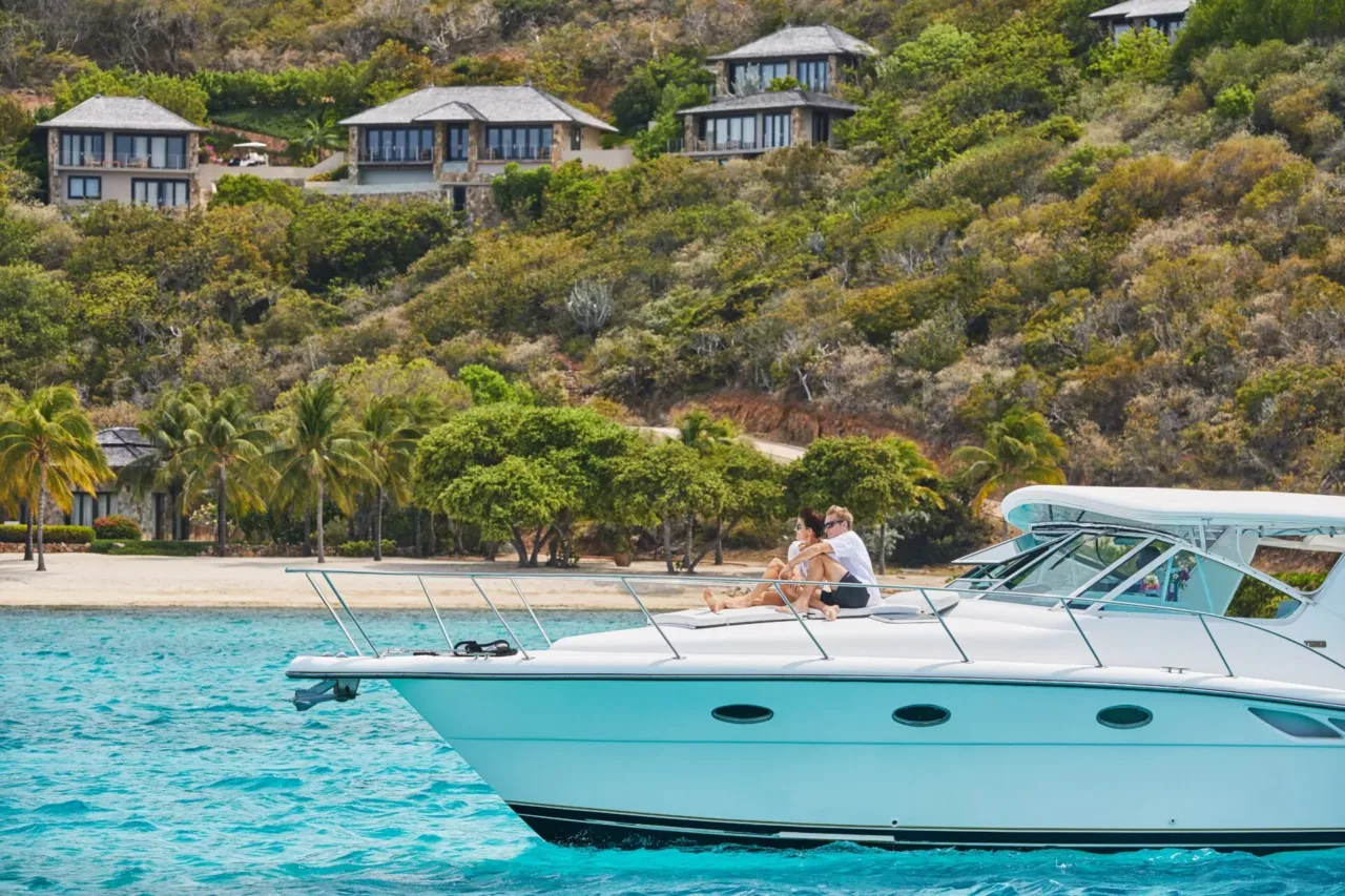 A couple takes in a spectacular view from the bow of a luxury yacht, cruising the vibrant deep blue waters past secluded villas nestled into the cliffs of Virgin Gorda.