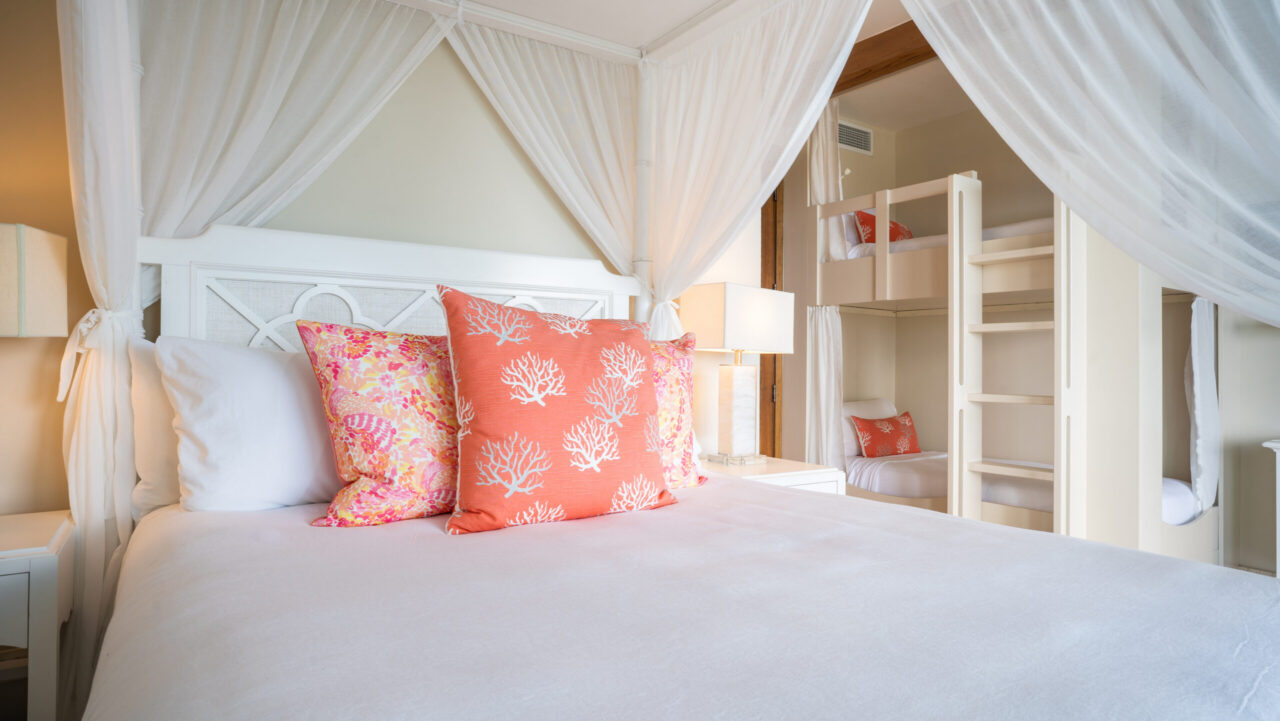 A primary bedroom in a luxury villa featuring a white four-poster canopy bed with views into an adjacent children's room equipped with custom-built white wooden bunk beds.