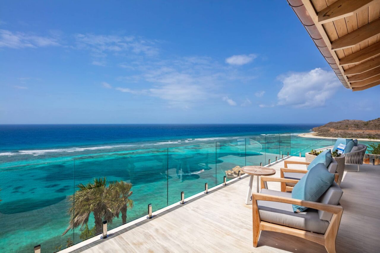 Bespoke luxury villa terrace at Oil Nut Bay featuring natural wood and upholstered outdoor armchairs overlooking the vibrant, reef-protected turquoise waters and pristine coastline of Virgin Gorda.