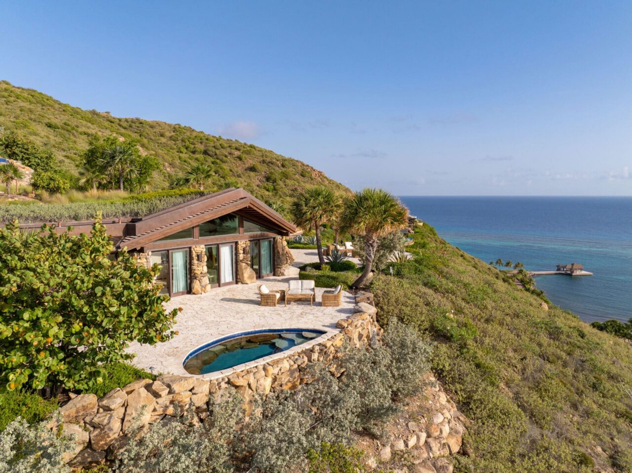 An aerial perspective of a low-density luxury estate at Oil Nut Bay, showcasing natural stone walls, a private infinity plunge pool, and a custom timber roofline completely surrounded by native island vegetation overlooking the Caribbean ocean.