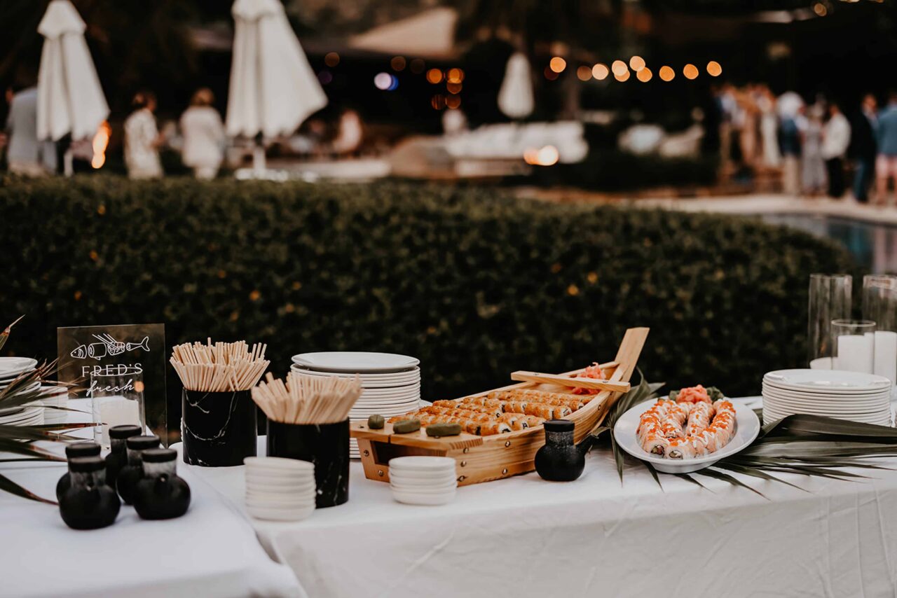 A luxury event catering station at Oil Nut Bay featuring a gourmet sushi buffet display elegantly presented on a wooden boat platter with polished table settings.