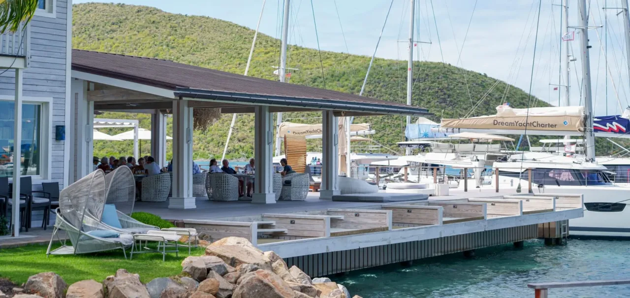 Exterior view of the al fresco dining pavilion at Nova Restaurant, highlighting premium open-air seating and integrated overwater daybeds extending over the sound alongside docked luxury yachts and catamarans.