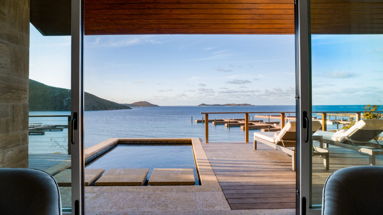 A luxury villa terrace at Oil Nut Bay Marina Village featuring a private plunge pool with stone stepping stones, wooden decking, chic lounge chairs, and an expansive view of the resort docks and calm turquoise waters of Virgin Gorda.