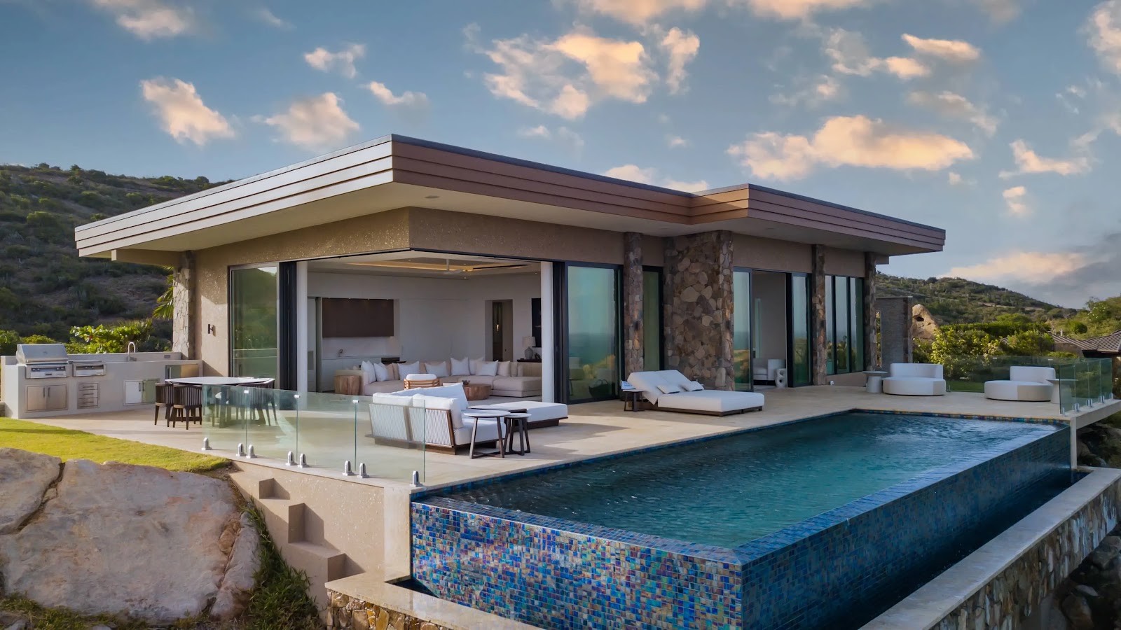 Modern cliffside villa featuring an expansive stone terrace, infinity pool, and open-air indoor lounge seating.