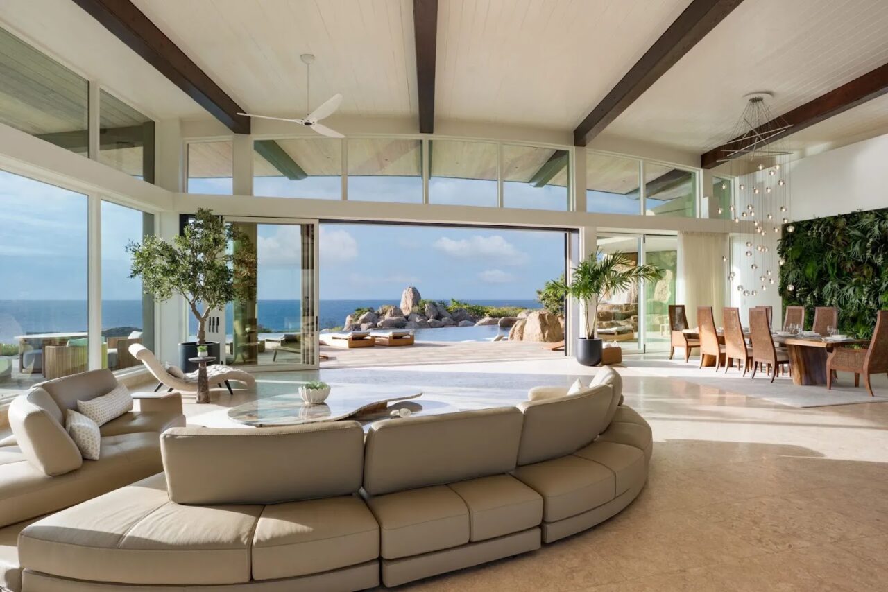 Sunlit Great Room in Halo Villa with floor-to-ceiling glass doors, curved leather sofa, and panoramic Caribbean views.