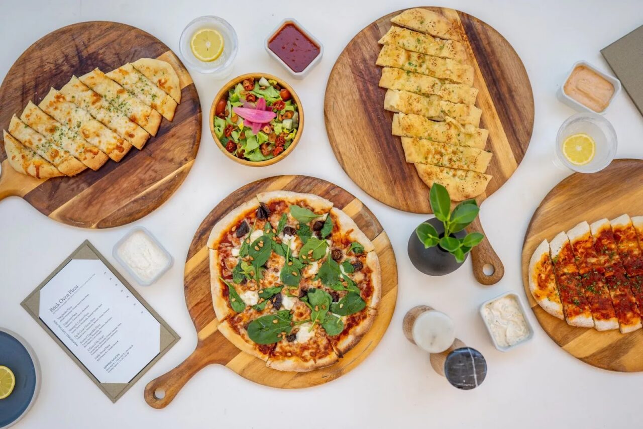 Overhead view of stone-oven pizzas, fresh salads, and flatbreads at The Beach Club at Oil Nut Bay.