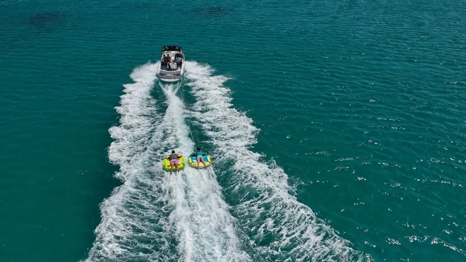 Aerial view of two guests tubing behind a boat in clear Caribbean waters