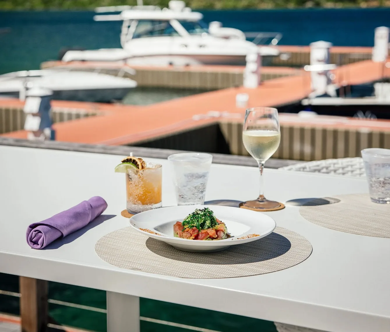 Fresh tuna poke bowl, craft cocktails, and wine set on an over-water table at Nova with North Sound marina views.