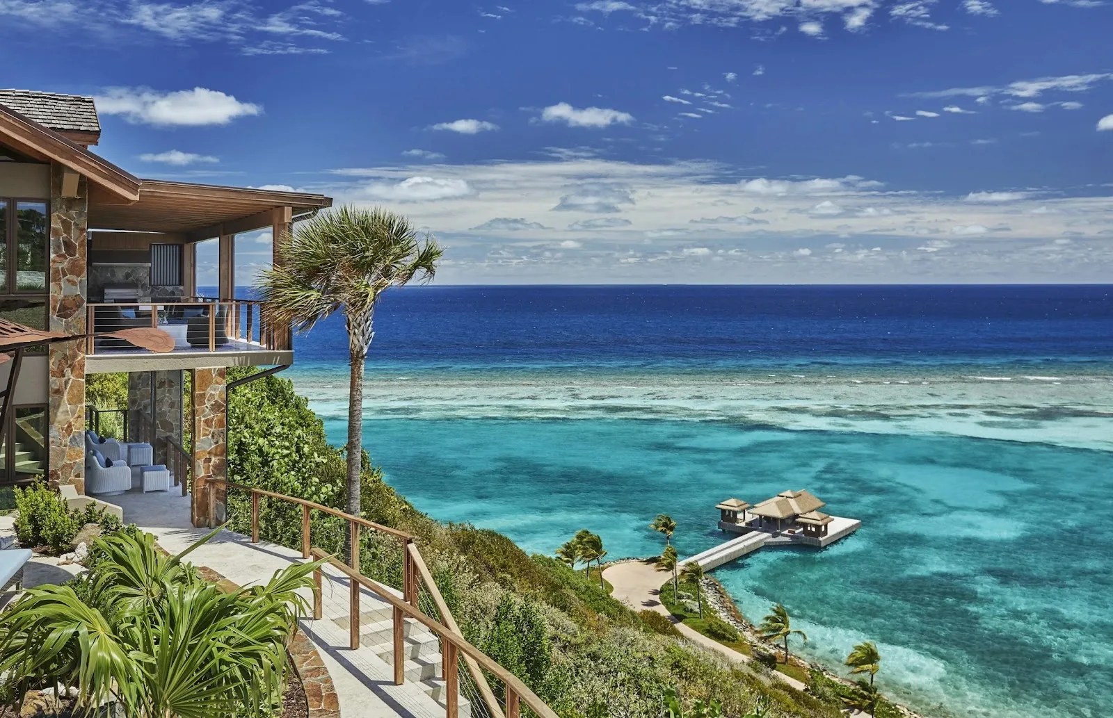 Luxury cliffside villa looking down at a private overwater dock in turquoise Caribbean waters.
