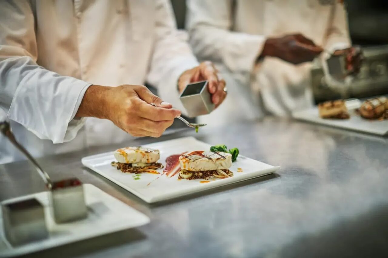 Oil Nut Bay resort chefs carefully plating gourmet grilled seafood dishes in a fine dining kitchen.
