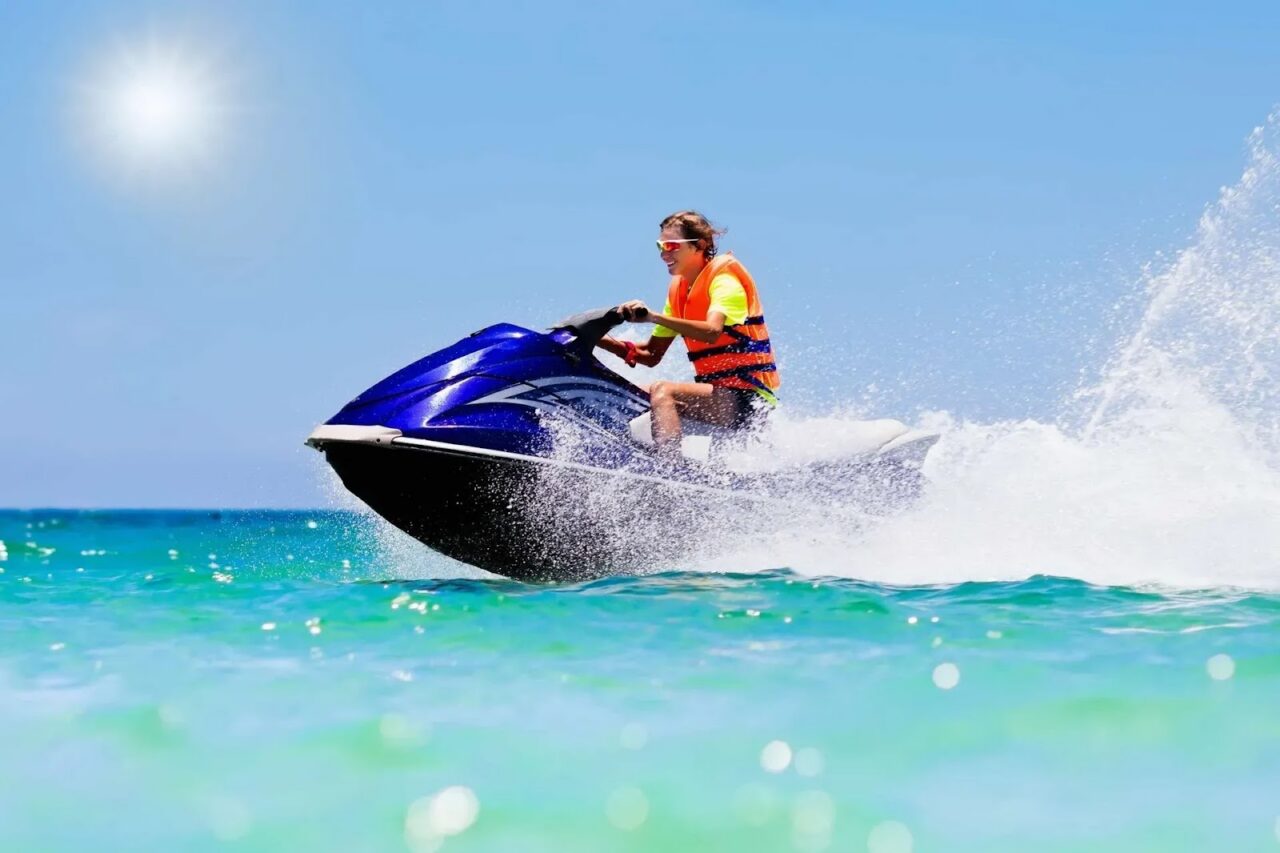 Man riding a blue jet ski across turquoise ocean waters near Oil Nut Bay